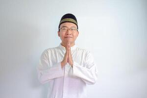 asiatisch Muslim Mann tragen Brille und Weiß Stoff lächelnd tun Gruß Pose zum Ramadhan und eid al fitr. isoliert Weiß Hintergrund foto