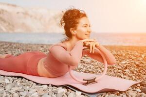 Frau Meer Pilates. sportlich glücklich Mitte alt Frau üben Fitness auf Strand in der Nähe von Meer, lächelnd aktiv weiblich Ausbildung mit Ring auf Yoga Matte außen, genießen gesund Lebensstil, Harmonie und Meditation foto