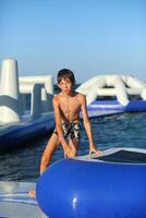kaukasisch Junge von neun Jahr alt haben Spaß beim das aufblasbar Strand aqua rutschen foto