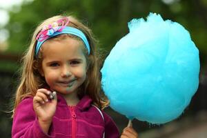 Nahansicht Porträt von glücklich Kleinkind Mädchen Essen hell Blau Baumwolle Süßigkeiten foto