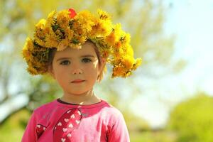 Frühling Porträt von ein süß zwei Jahre alt Mädchen posieren mit ein Löwenzahn Kranz foto