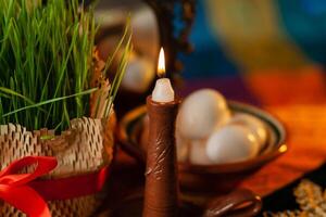 ein Kerze brennt auf ein festlich Tabelle in der Nähe von Weizen Keim, ein Spiegel, Eier. traditionell Symbole von iranisch persisch Neu Jahr nevruz, Nahansicht foto