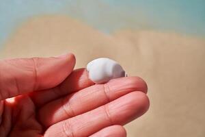 ein Abstrich von Weiß Sahne mit spf auf das Finger gegen ein Hintergrund von Sand. foto