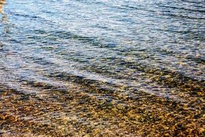 Hintergrund von das Wasser von See traunsee im das Küsten Bereich. bunt Textur von Steine unter Wasser. foto