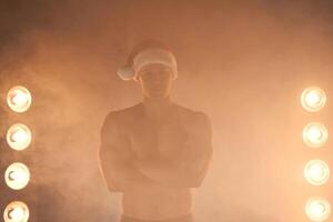 Porträt von muskulös Mann tragen Weihnachten Santa Hut, gefaltet Hände auf rauchig Hintergrund foto