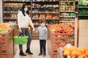 jung Frau und ihr Kind tragen schützend Gesicht Masken Geschäft ein Essen beim ein Supermarkt während das Coronavirus Epidemie oder Grippe Ausbruch. foto