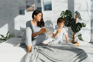 Mama mit Sohn im Pyjama Trinken Saft im das Morgen im Bett. gesund Essen Konzept foto