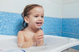 Spaß heiter glücklich Kleinkind Baby nehmen ein Bad spielen mit Schaum Blasen. wenig Kind im ein Badewanne. lächelnd Kind im Badezimmer auf Blau Hintergrund. Hygiene und Gesundheit Pflege. foto