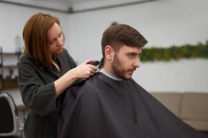 gut aussehend Blau Augen Mann Sitzung im Barbier Geschäft. Friseur Friseur Frau Schneiden seine Haar. weiblich Barbier. foto