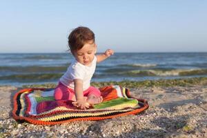 wenig Kind Sitzung auf ein farbig Teppich auf das Strand heiter und glücklich foto