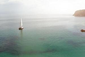 Panorama- Aussicht von Pazifik Ozean Blau transparent Wasser, ein Weiß Sport modern Luxus Yacht segeln Boot schwebend und ein Grün Ufer mit Wald, Hügel. Urlaub durch das Wasser und segeln Wettrennen. foto