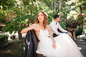 ein schön Braut im ein Weiß Hochzeit Kleid und Kranz sitzt auf ein Stuhl Nächster zu das Bräutigam, ruhen und vorbereiten zum ein glücklich Familie Leben foto