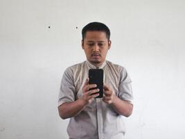 Erwachsene asiatisch Mann SMS auf seine Handy, Mobiltelefon Telefon mit ernst Ausdruck foto