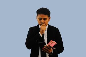 Erwachsene asiatisch Mann tun Denken Geste während halten Indonesien Papier Geld foto
