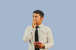 Erwachsene asiatisch Mann tun Denken Geste während halten Indonesien Papier Geld foto