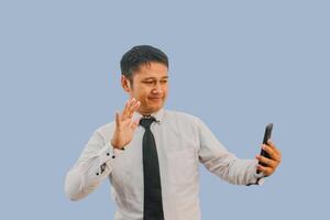Erwachsene asiatisch Mann winken Hand mit glücklich Gesicht Ausdruck während Video Anruf foto