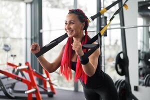 Athlet Frau Ausbildung ausüben mit Suspension System Innen- Fitnessstudio. schön kaukasisch sportlich Frau tun Dehnen Stärke Übung mit Besondere Gurt foto