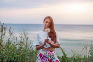 glücklich schön Frau weht Löwenzahn Über Himmel und Meer Hintergrund, haben Spaß und spielen draussen, Teen Mädchen genießen Natur, Sommer- Ferien und Feiertage, jung ziemlich weiblich halten Blume foto