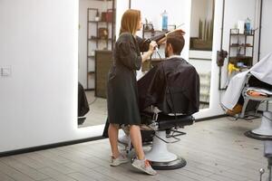 gut aussehend Blau Augen Mann Sitzung im Barbier Geschäft. Friseur Friseur Frau Schneiden seine Haar. weiblich Barbier. foto