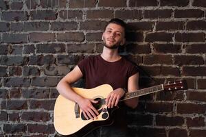 Mann mit akustisch Gitarre gegen Backstein Mauer spielen Musik- Singen Lieder genießen Leben Mittel schießen foto