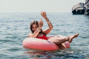 Frau Sommer- Meer. glücklich Frau Schwimmen mit aufblasbar Krapfen auf das Strand im Sommer- sonnig Tag, umgeben durch vulkanisch Berge. Sommer- Ferien Konzept. foto