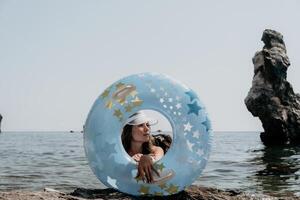 Frau Sommer- Meer. glücklich Frau Schwimmen mit aufblasbar Krapfen auf das Strand im Sommer- sonnig Tag, umgeben durch vulkanisch Berge. Sommer- Ferien Konzept. foto