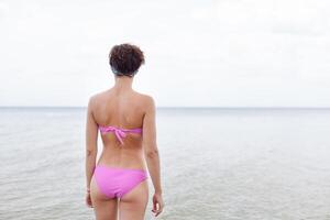 Rückseite Aussicht von jung Frau im Bikini Laufen auf das Strand. kaukasisch weiblich Modell- auf das Meer Ufer. foto