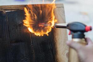 Fachmann Zimmermann mit alt traditionell japanisch Technik. Verbrennung Holz Bretter mit Gas Brenner foto