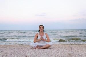 Frau Praktiken Methoden Ausübungen Yoga und meditiert im das Lotus Position auf das Strand foto