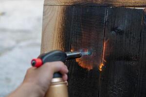 Fachmann Zimmermann mit alt traditionell japanisch Technik. Verbrennung Holz Bretter mit Gas Brenner foto