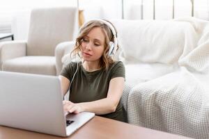 Frau Brille mit Laptop Computer während Sitzung in der Nähe von Sofa mit groß Fenster auf Hintergrund beim Zuhause Innere foto