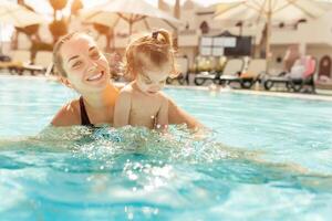 Mama und wenig Tochter sind gespielt im das öffnen Schwimmen Schwimmbad. Familie mit einer Kind auf Ferien im warm Länder. positiv Menschen auf Urlaub. foto