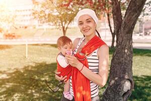 Mutter tragen ein Säugling Baby im wickeln Schlinge im Park. Frühling. Konzept von natürlich Erziehung foto