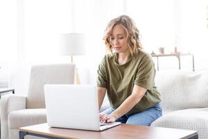 Frau mit Laptop Computer während Sitzung Sofa mit groß Fenster auf Hintergrund beim Zuhause Innere foto