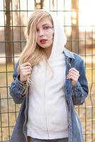 jung Frau mit vorübergehend gemalt Blumen auf das Gesicht. Teenager Mädchen mit lange blond Haar tragen Jeans Jacke und Hoody foto