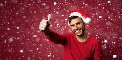 jung gut aussehend kaukasisch Kerl im ein rot Sweatshirt und Santa Hüte steht auf rot Hintergrund im Studio und zeigen Daumen hoch. foto