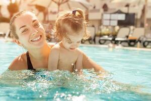 Mama und wenig Tochter sind gespielt im das öffnen Schwimmen Schwimmbad. Familie mit einer Kind auf Ferien im warm Länder. positiv Menschen auf Urlaub. foto