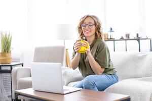 Frau Brille mit Laptop Computer während Sitzung Sofa mit groß Fenster auf Hintergrund beim Zuhause Innere foto