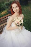 Braut im elegant Hochzeit Kleid sitzt auf Stein Bank foto