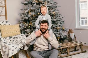 Urlaub Weihnachten gut aussehend Vater spielen mit klein süß Sohn in der Nähe von dekoriert Neu Jahr Baum beim Zuhause foto