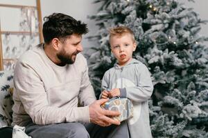 Urlaub Weihnachten gut aussehend Vater spielen mit klein süß Sohn in der Nähe von dekoriert Neu Jahr Baum beim Zuhause foto