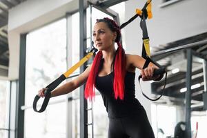 Athlet Frau Ausbildung ausüben mit Suspension System Innen- Fitnessstudio. schön kaukasisch sportlich Frau tun Dehnen Stärke Übung mit Besondere Gurt foto