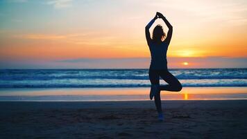 Silhouette Frau trainieren Yoga Baum Pose zu Meditation mit Sommer- Ferien Strand Glück und Entspannung. Ruhe weiblich Übung mit Yoga meditieren Ozean Strand mit Sonnenuntergang golden Zeit. foto