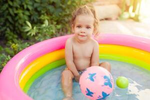 Kinder spielen im aufblasbar Baby Schwimmbad. Kinder schwimmen und Spritzen im bunt Garten abspielen Center. glücklich wenig Mädchen spielen mit Wasser Spielzeuge auf heiß Sommer- Tag. Familie haben Spaß draußen im das Hinterhof. foto