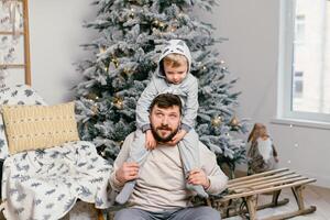 Urlaub Weihnachten gut aussehend Vater spielen mit klein süß Sohn in der Nähe von dekoriert Neu Jahr Baum beim Zuhause foto