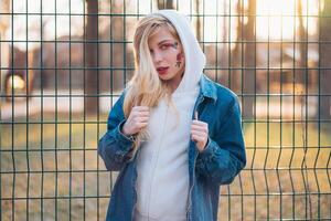 jung Frau mit vorübergehend gemalt Blumen auf das Gesicht. Teenager Mädchen mit lange blond Haar tragen Jeans Jacke und Hoody foto