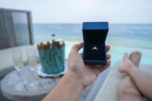 Hand halten ein Box mit Engagement Ring mit Ozean Aussicht Hintergrund. foto