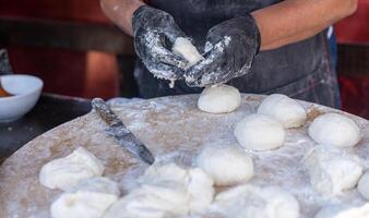 Koch im schwarz Handschuhe schneidet roh Teig in Stücke machen Pizza Pastetchen Brot. foto