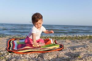 glücklich Baby lächelnd und winken Hand, Sitzung auf Weiß sandig tropisch Strand auf das Teppich foto