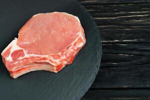 oben Aussicht von einer Stücke roh Schweinefleisch hacken Steaks auf ein schwarz Stein Schneiden Tafel. foto